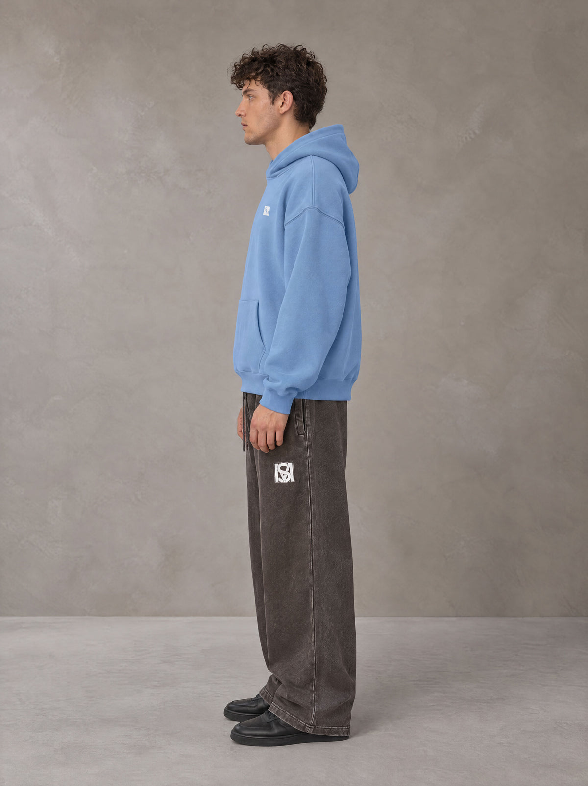Model wearing SM Sig. Fleece Hoodie in Soft Blue, side profile.