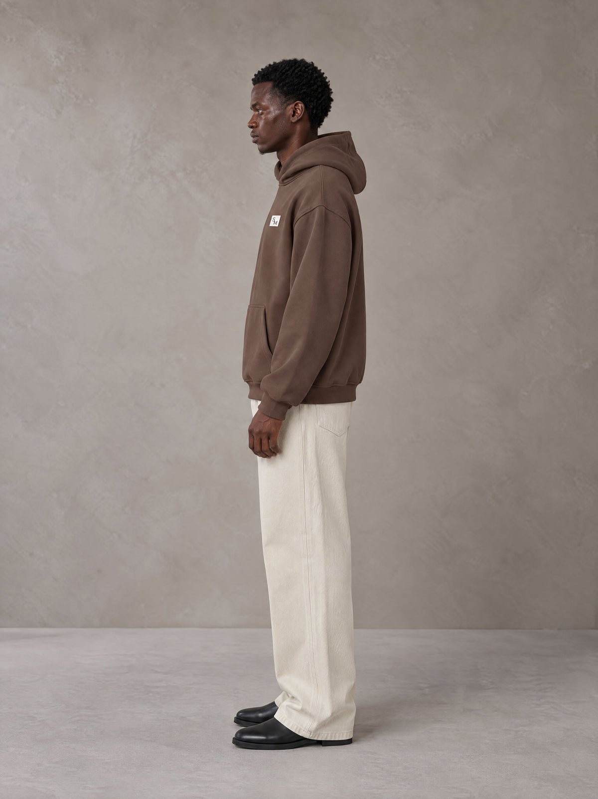 Model wearing SM Sig. High Neck Fleece Hoodie in Brown, side profile.