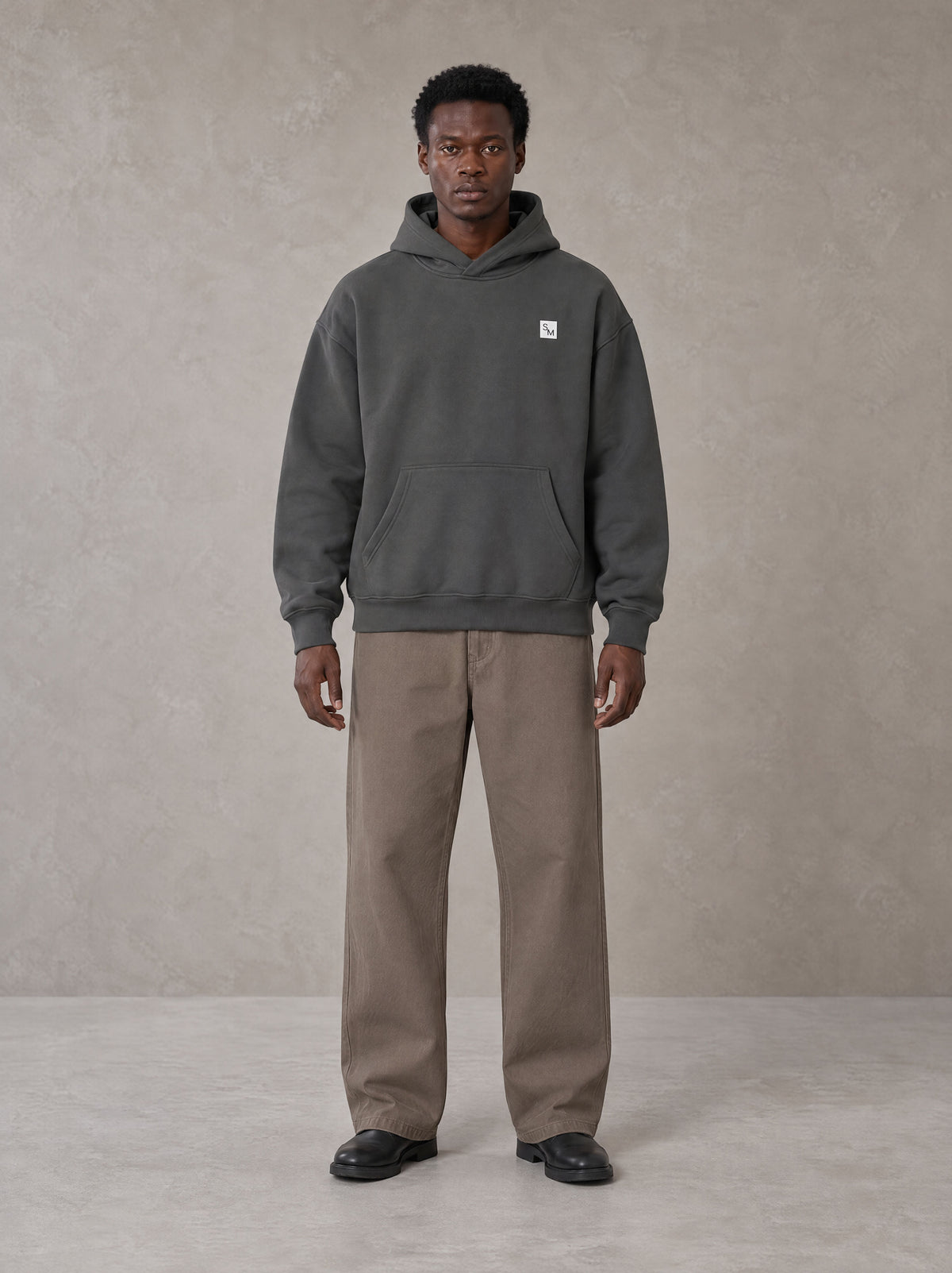 Model wearing SM Sig. High Neck Fleece Hoodie in Deep Charcoal, front view.
