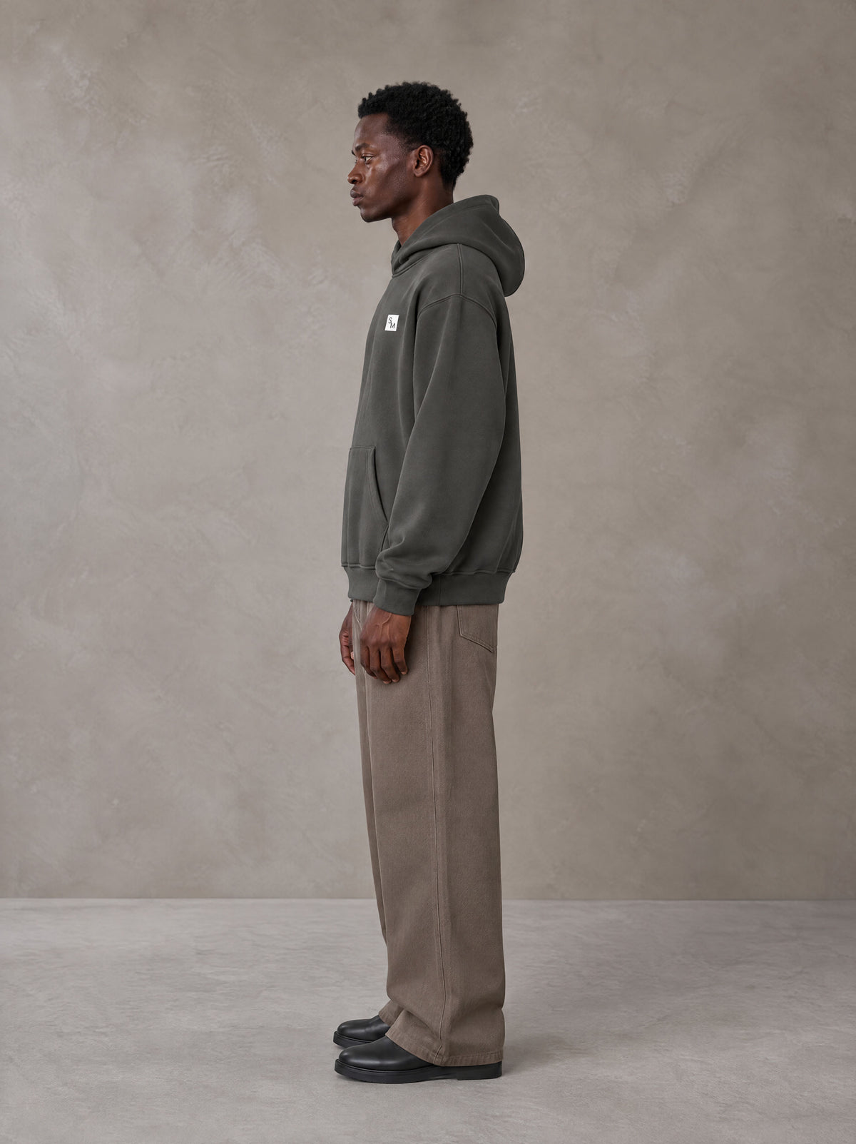 Model wearing SM Sig. High Neck Fleece Hoodie in Deep Charcoal, side profile.