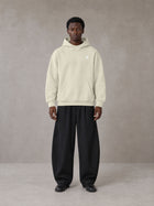 Model wearing SM Sig. High Neck Fleece Hoodie in Fine Sand, front view.