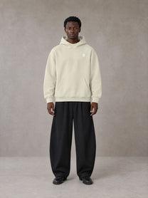 Model wearing SM Sig. High Neck Fleece Hoodie in Fine Sand, front view.