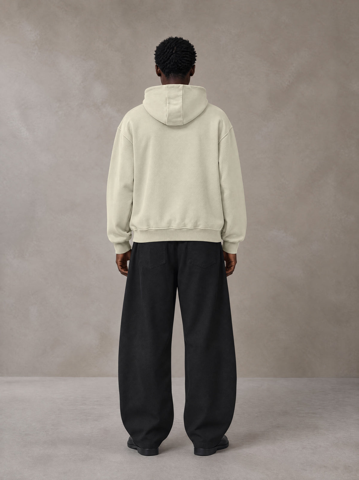 Model wearing SM Sig. High Neck Fleece Hoodie in Fine Sand, rear view.