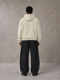 Model wearing SM Sig. High Neck Fleece Hoodie in Fine Sand, rear view.