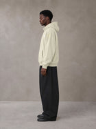 Model wearing SM Sig. High Neck Fleece Hoodie in Fine Sand, side profile.