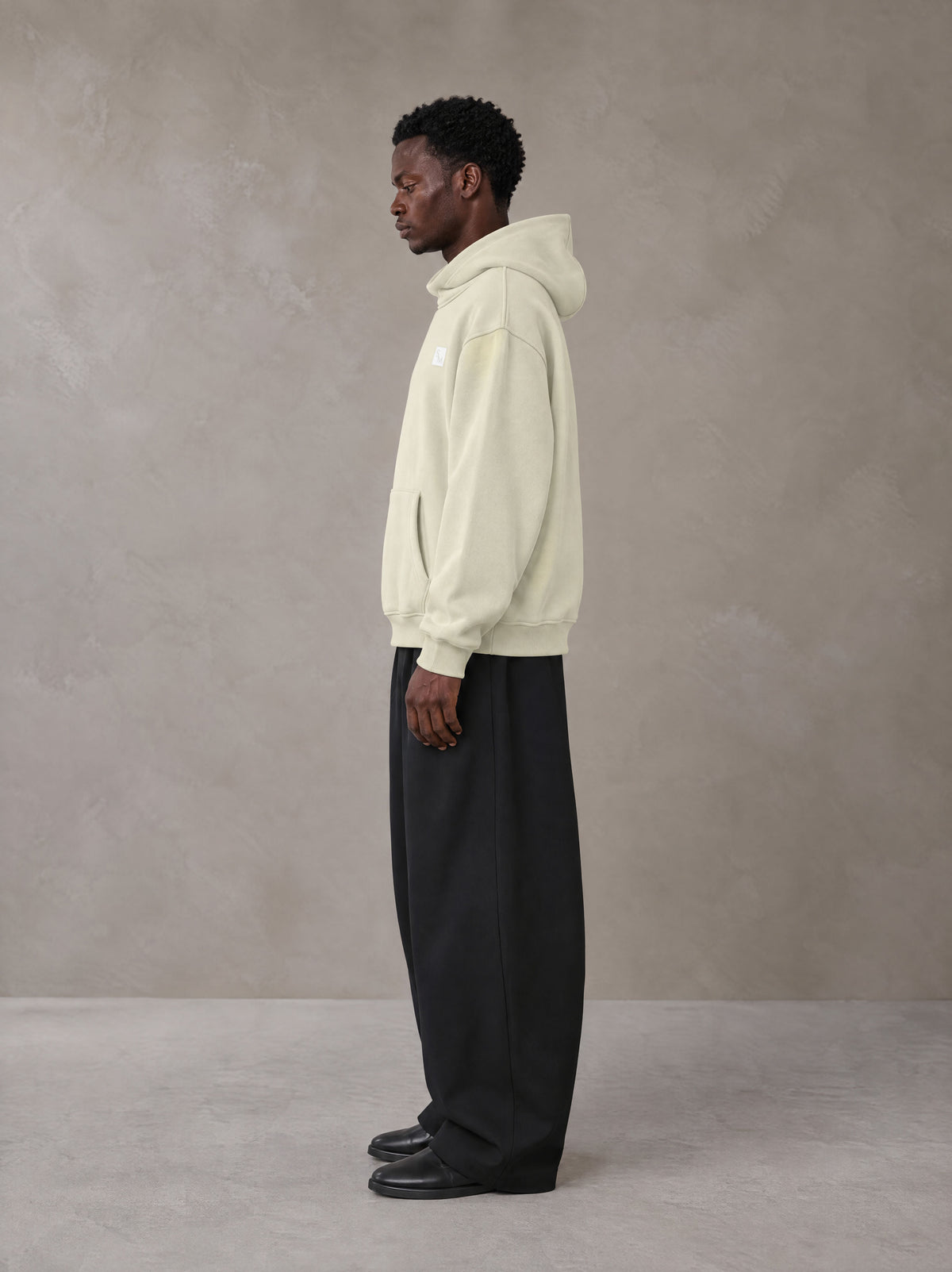 Model wearing SM Sig. High Neck Fleece Hoodie in Fine Sand, side profile.