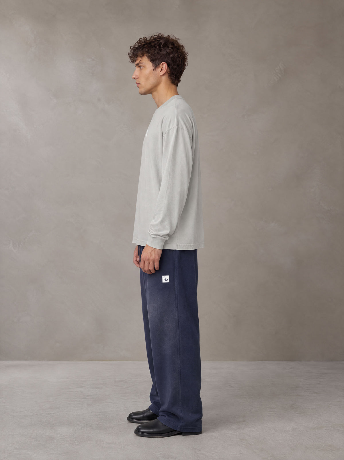 Model wearing SM Sig. Long Sleeve T-shirt in Pure Grey, side profile.