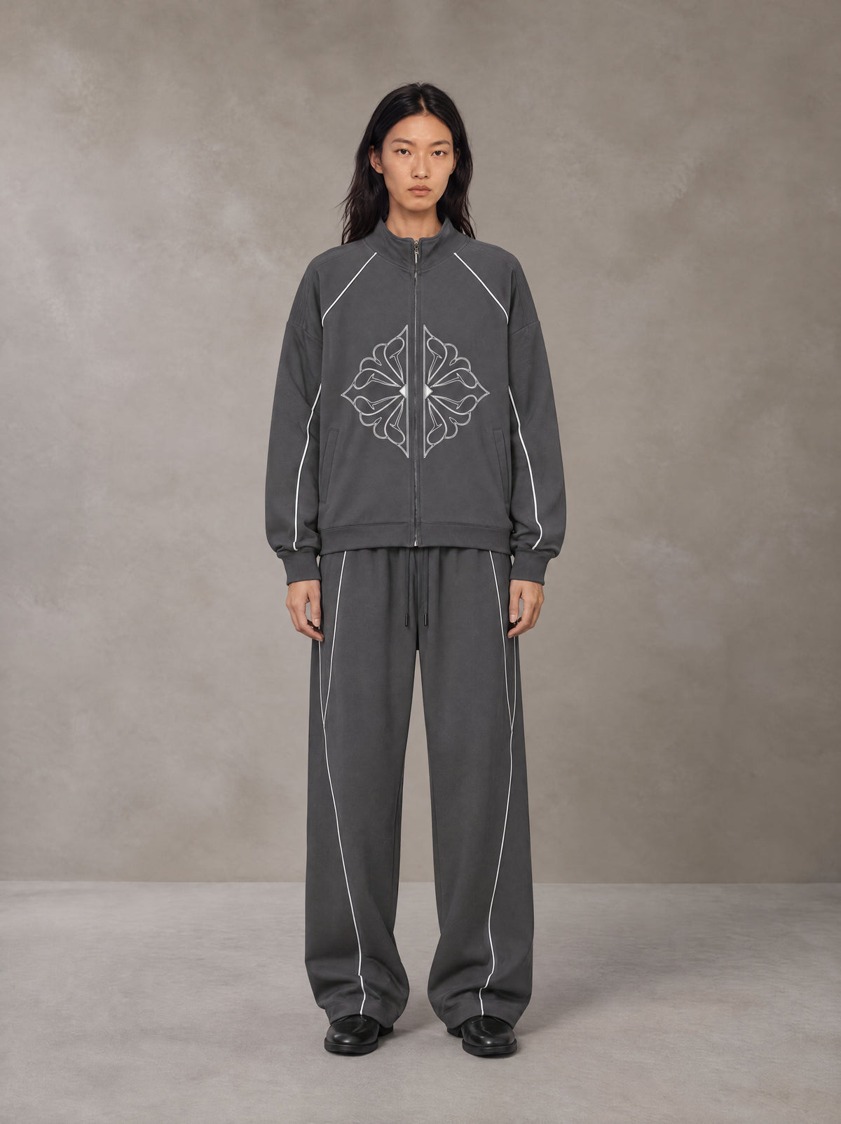 Model wearing the SM Fleur Eclipse Jacket and SM Fleur Eclipse Sweatpants in Deep Charcoal, front view.