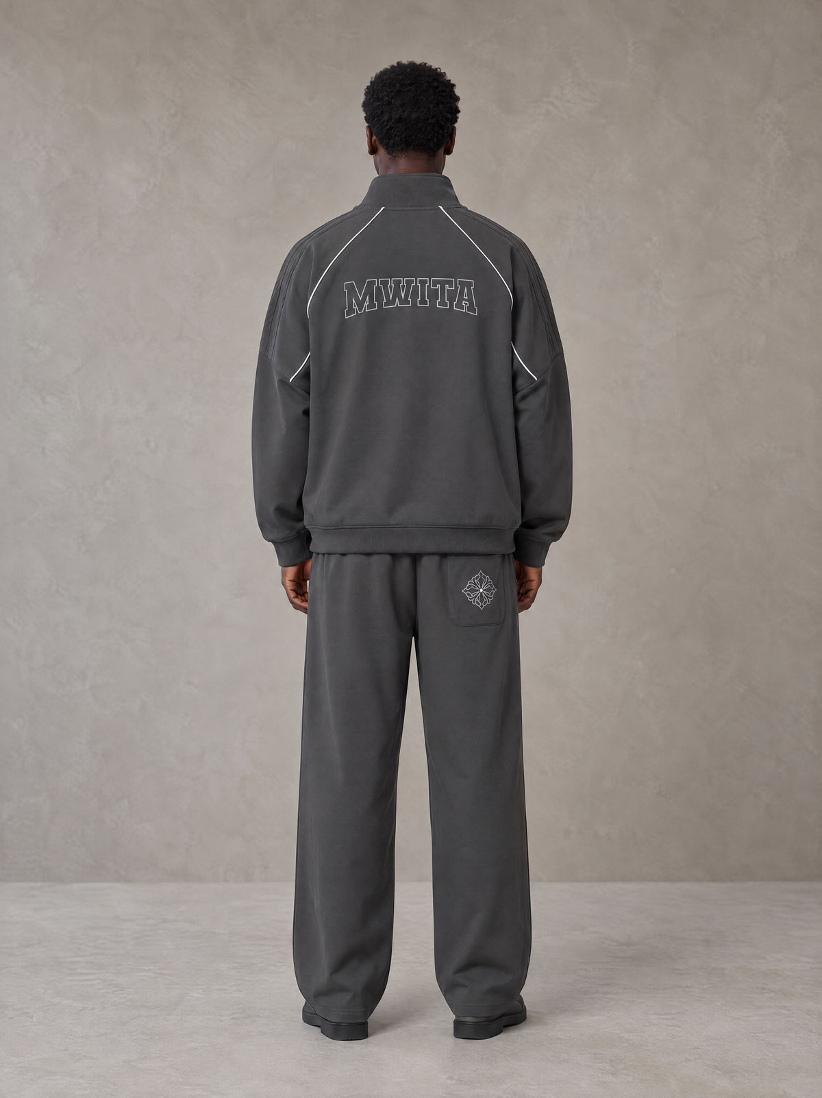 Model wearing the SM Fleur Eclipse Jacket and SM Fleur Eclipse Sweatpants in Deep Charcoal, rear view.