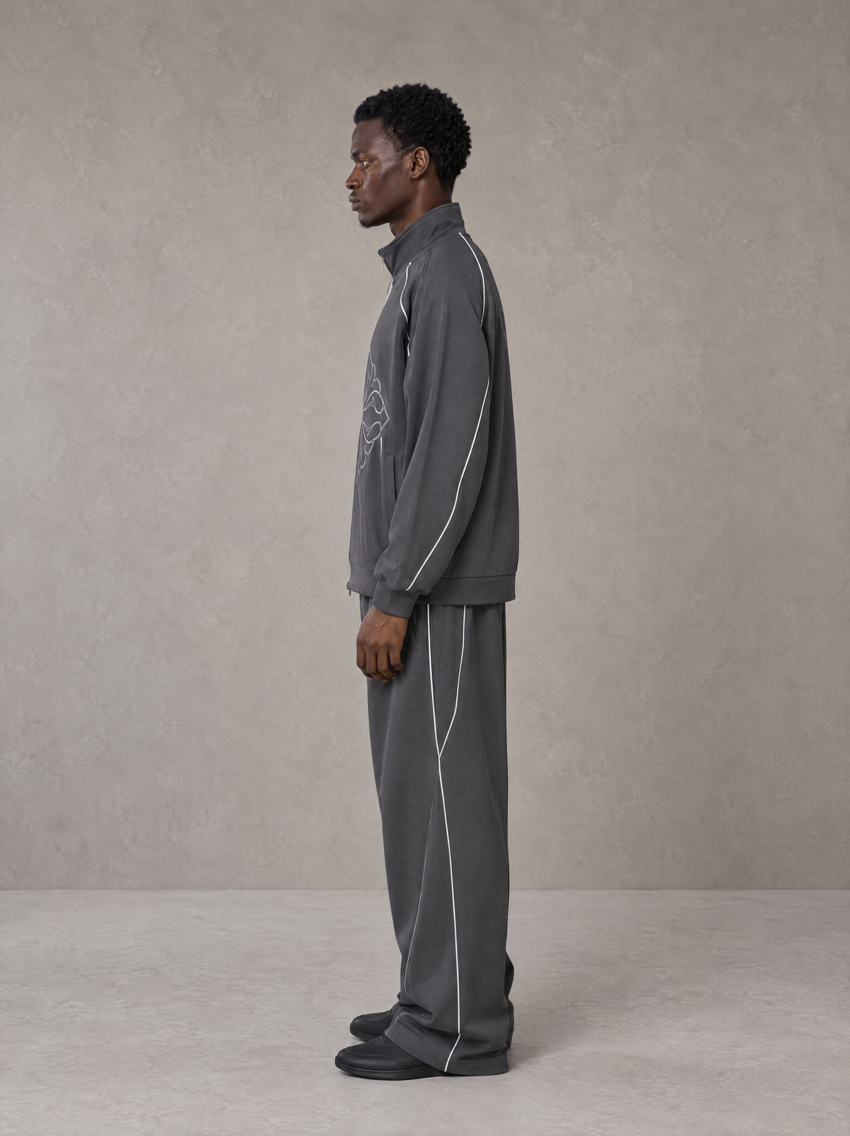 Model wearing the SM Fleur Eclipse Jacket and SM Fleur Eclipse Sweatpants in Deep Charcoal, side profile.