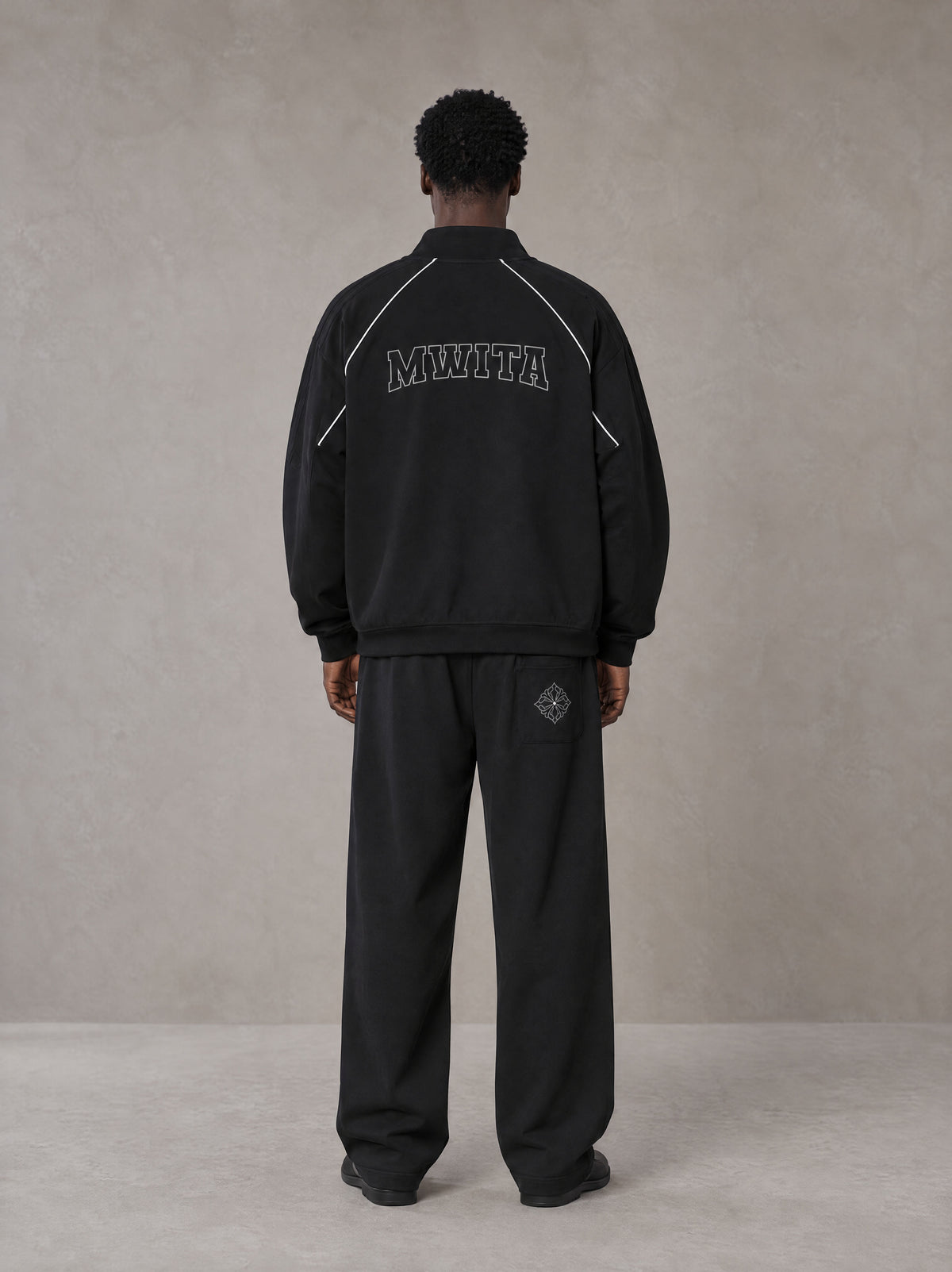 Model wearing the SM Fleur Eclipse Jacket and SM Fleur Eclipse Sweatpants in Midnight Black, rear view.