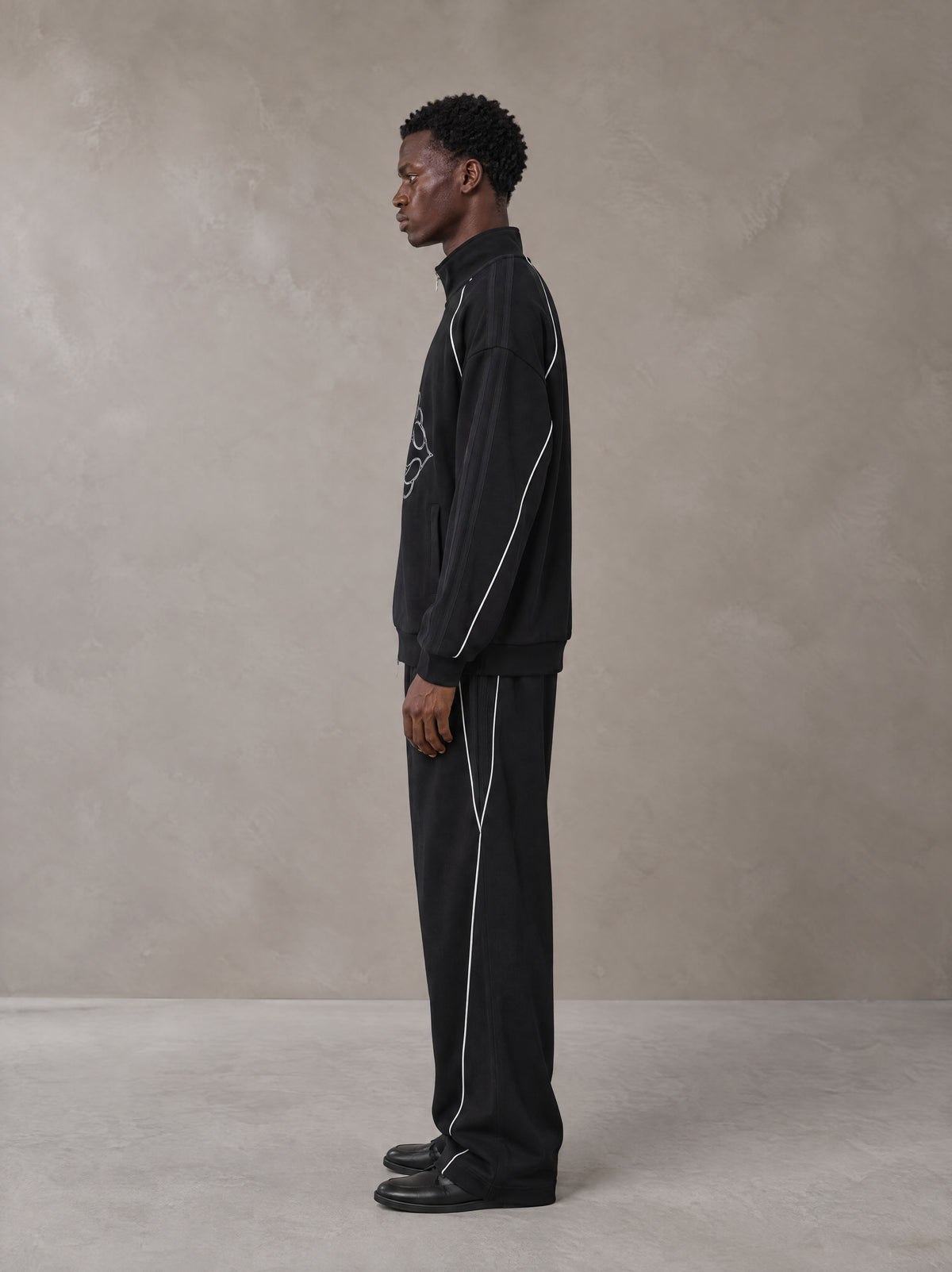Model wearing the SM Fleur Eclipse Jacket and SM Fleur Eclipse Sweatpants in Midnight Black, side profile.