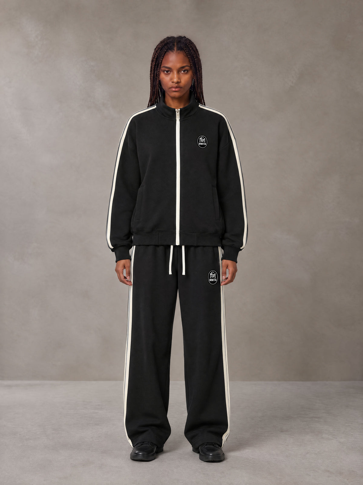 Model wearing the SM Insignia Track Jacket and SM Insignia Track Trousers in Midnight Black, front view.