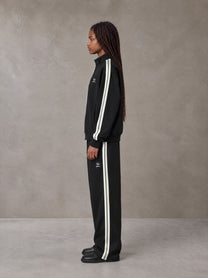 Model wearing the SM Insignia Track Jacket and SM Insignia Track Trousers in Midnight Black, side profile.