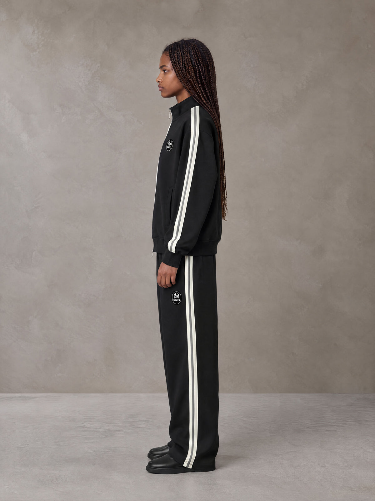 Model wearing the SM Insignia Track Jacket and SM Insignia Track Trousers in Midnight Black, side profile.