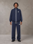 Model wearing the SM Insignia Track Jacket and SM Insignia Track Trousers in Oxford Navy, front view.