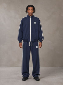 Model wearing the SM Insignia Track Jacket and SM Insignia Track Trousers in Oxford Navy, front view.