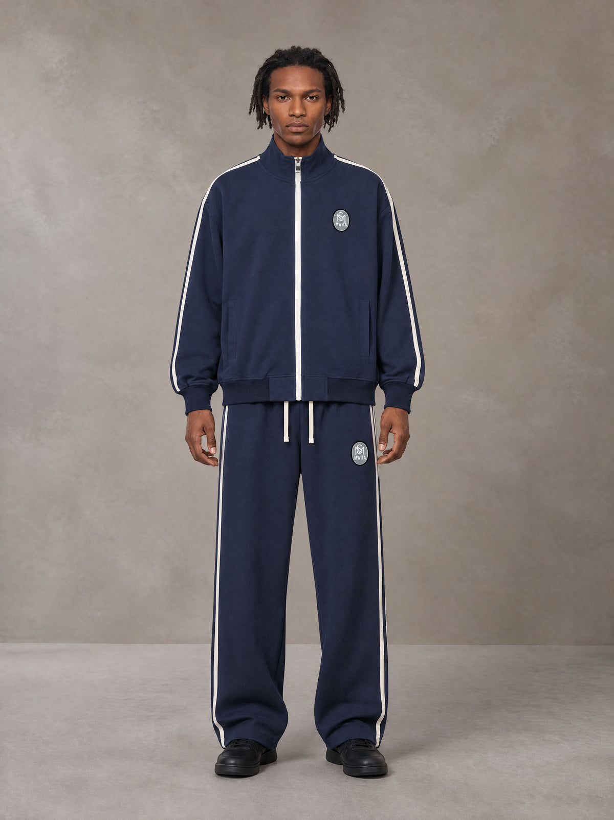 Model wearing the SM Insignia Track Jacket and SM Insignia Track Trousers in Oxford Navy, front view.