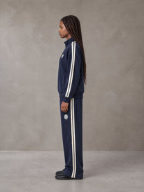 Model wearing the SM Insignia Track Jacket and SM Insignia Track Trousers in Oxford Navy, side profile.
