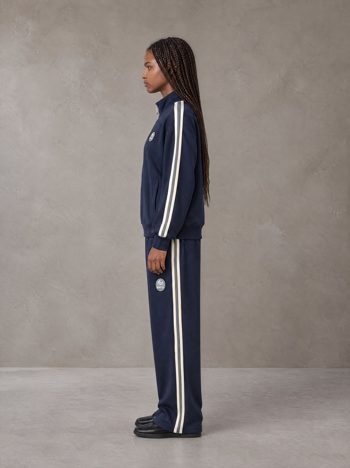 Model wearing the SM Insignia Track Jacket and SM Insignia Track Trousers in Oxford Navy, side profile.