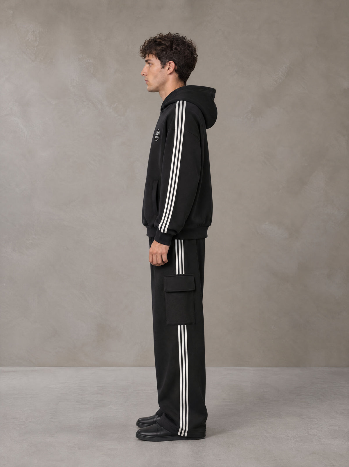 Model wearing the SM Insignia Utility Hoodie and SM Insignia Utility Sweatpants in Midnight Black, side profile.
