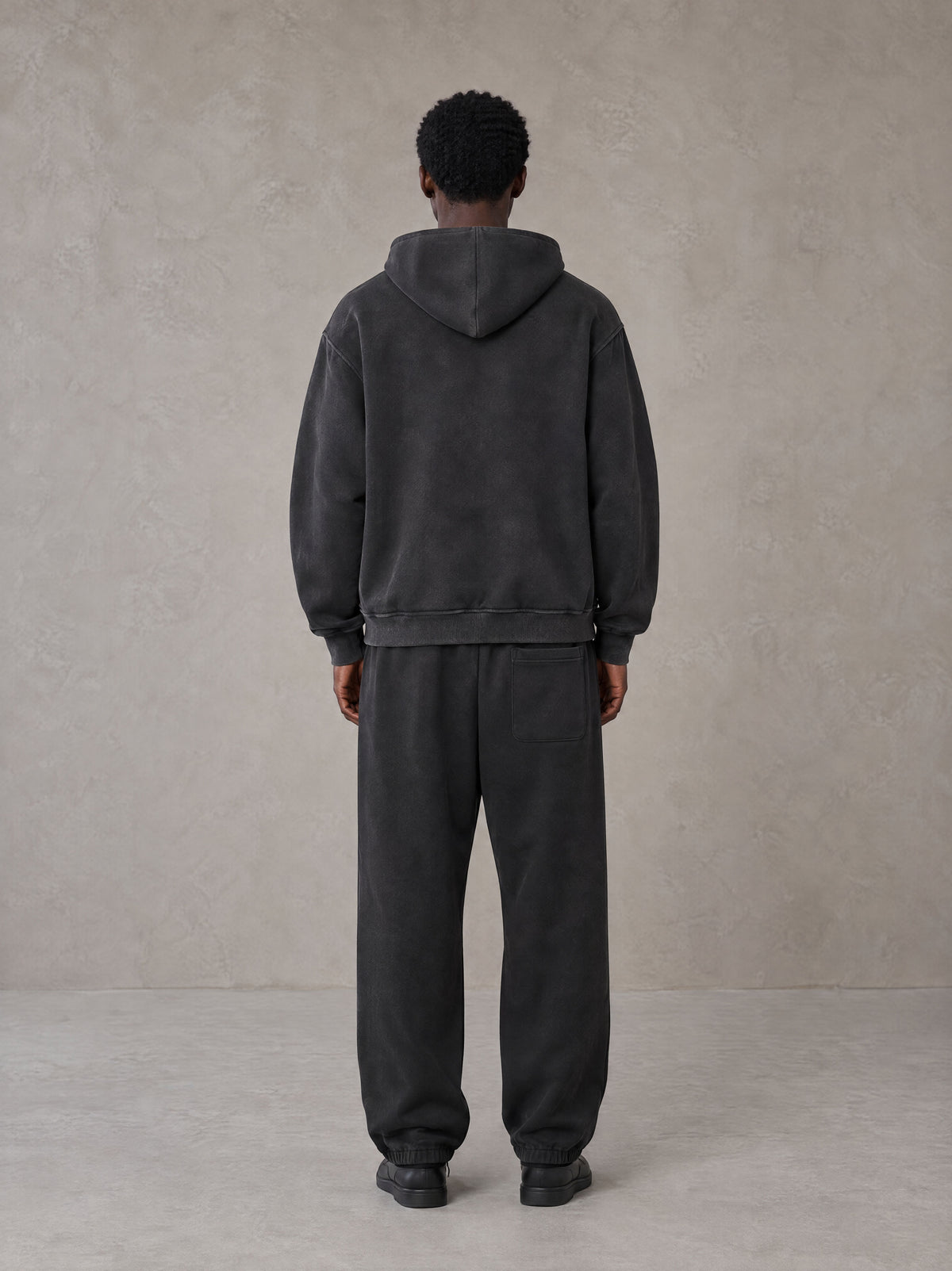 Model wearing the SM Track Line Hoodie and SM Track Line Sweatpants in Midnight Black, rear view.