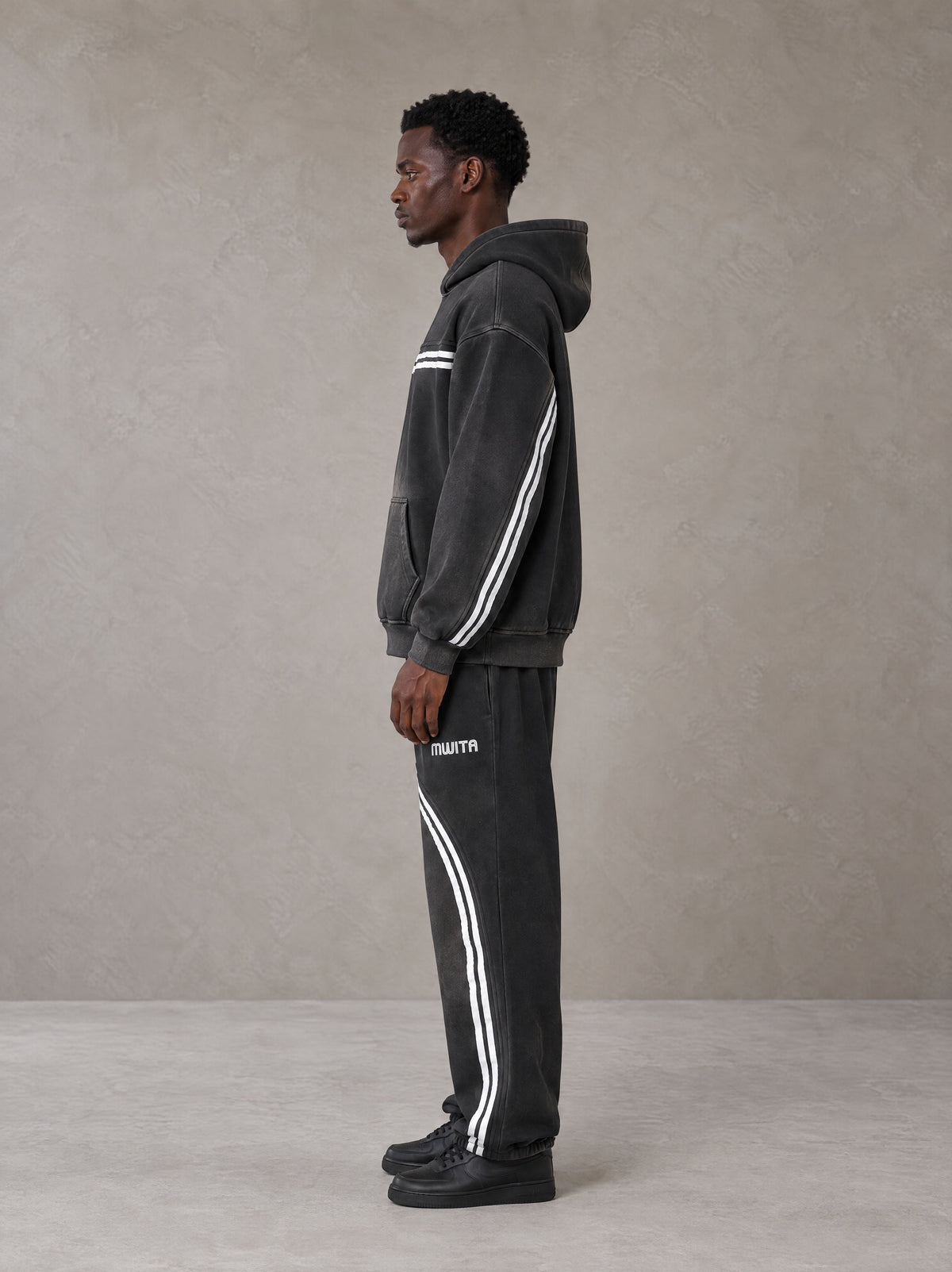 Model wearing the SM Track Line Hoodie and SM Track Line Sweatpants in Midnight Black, side profile.