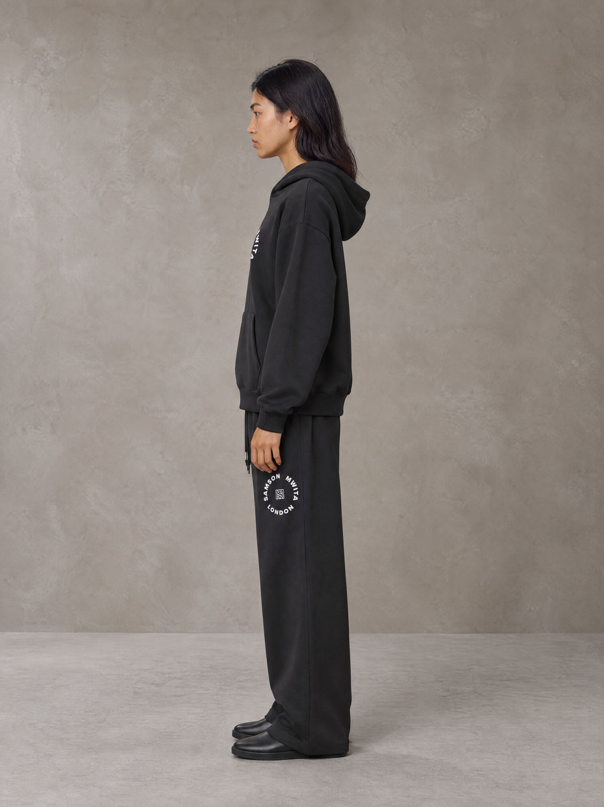 Model wearing the SM London Hoodie and SM London Sweatpants in Deep Charcoal, side profile.
