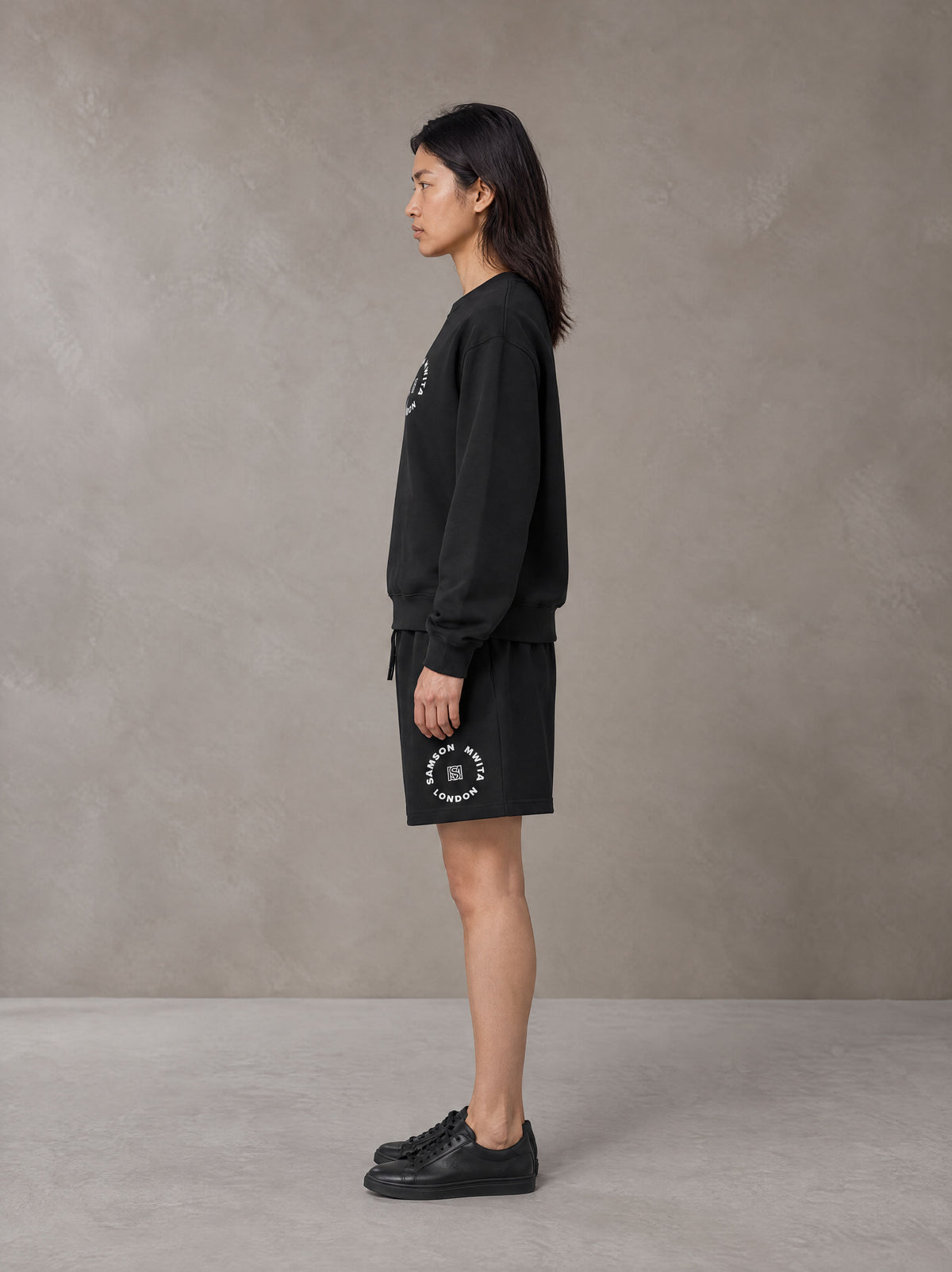 Model wearing the SM London Sweatshirt and SM London Shorts in Midnight Black, side profile.