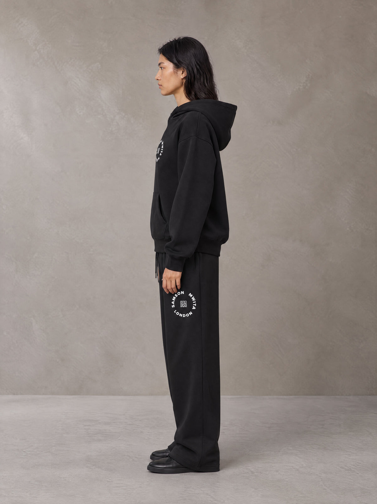 Model wearing the SM London Hoodie and SM London Sweatpants in Midnight Black, side profile.