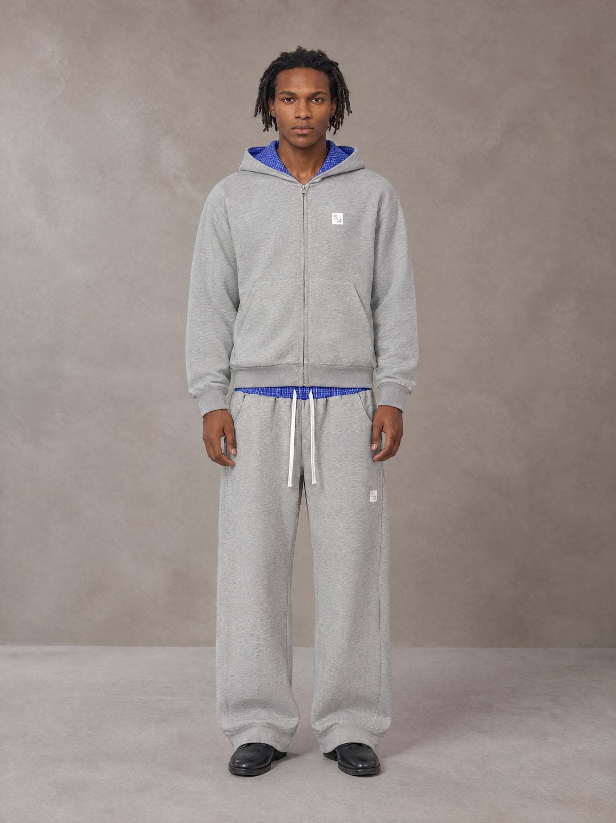 Model wearing the SM Sig. Plaid Zip Hoodie and SM Sig. Plaid Sweatpants in Floral Grey, front view.