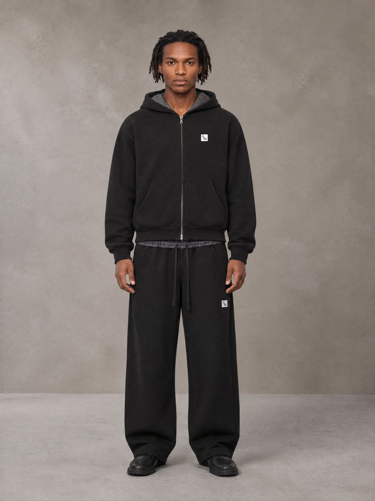 Model wearing the SM Sig. Plaid Zip Hoodie and SM Sig. Plaid Sweatpants in Midnight Black, front view.