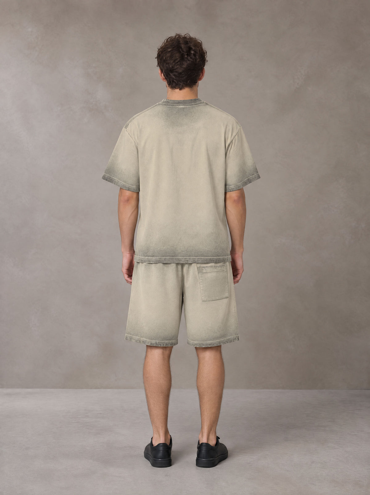 Model wearing the SM Sig. Reverse Dyed T-shirt and SM Sig. Reverse Dyed Shorts in Fine Sand, rear view.