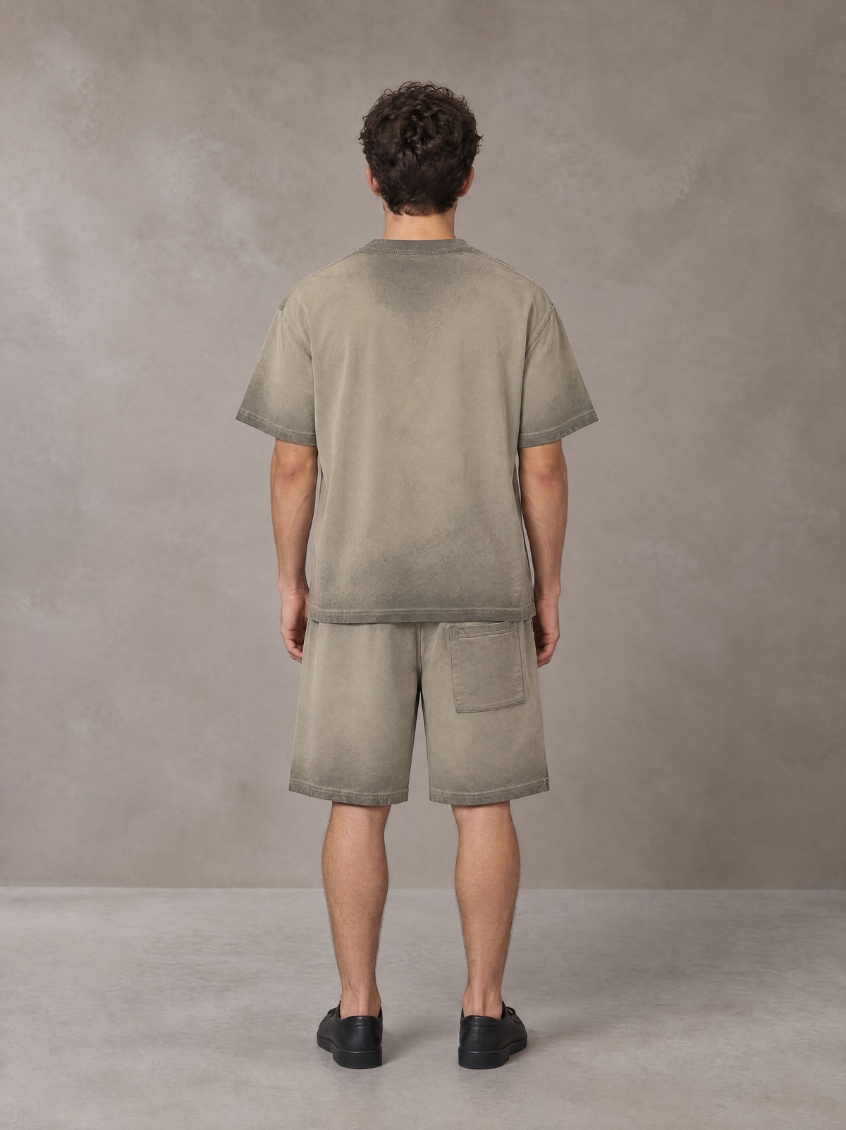 Model wearing the SM Sig. Reverse Dyed T-shirt and SM Sig. Reverse Dyed Shorts in Stone Grey, rear view.