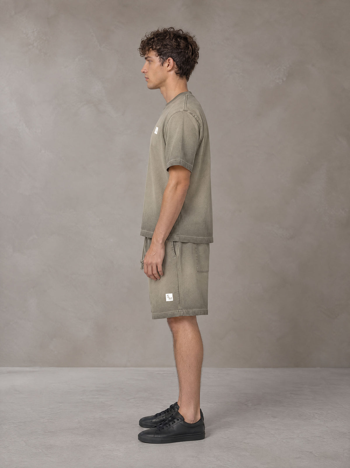 Model wearing the SM Sig. Reverse Dyed T-shirt and SM Sig. Reverse Dyed Shorts in Stone Grey, side profile.