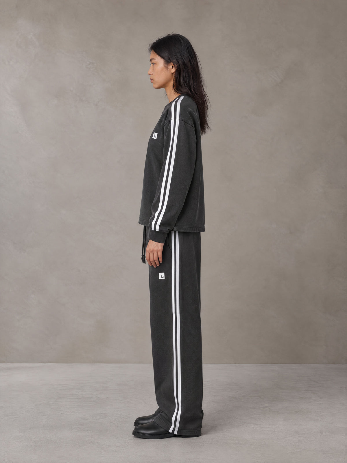 Model wearing the SM Sig. Snow Line Sweatshirt and SM Sig. Snow Line Sweatpants in Midnight Black, side profile.