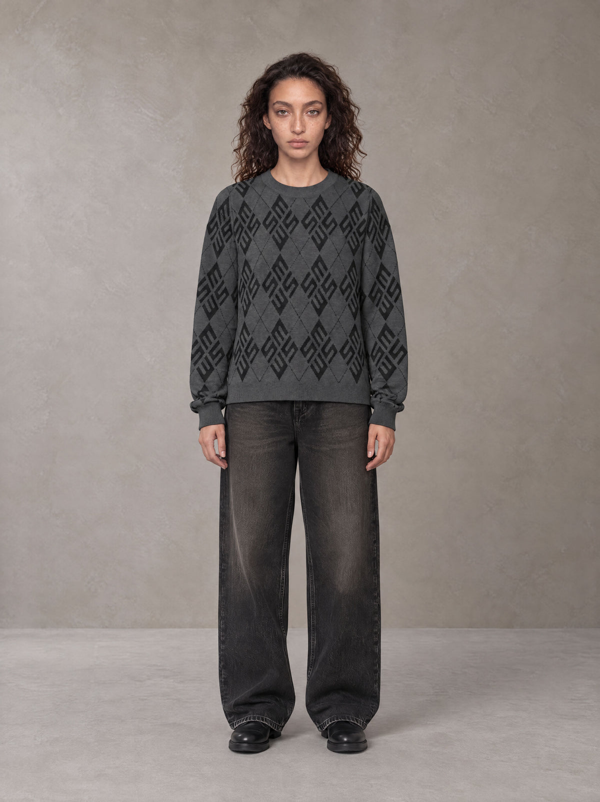 Model wearing the SM Argyle Jacquard Knitted Sweatshirt in Deep Charcoal, front view.