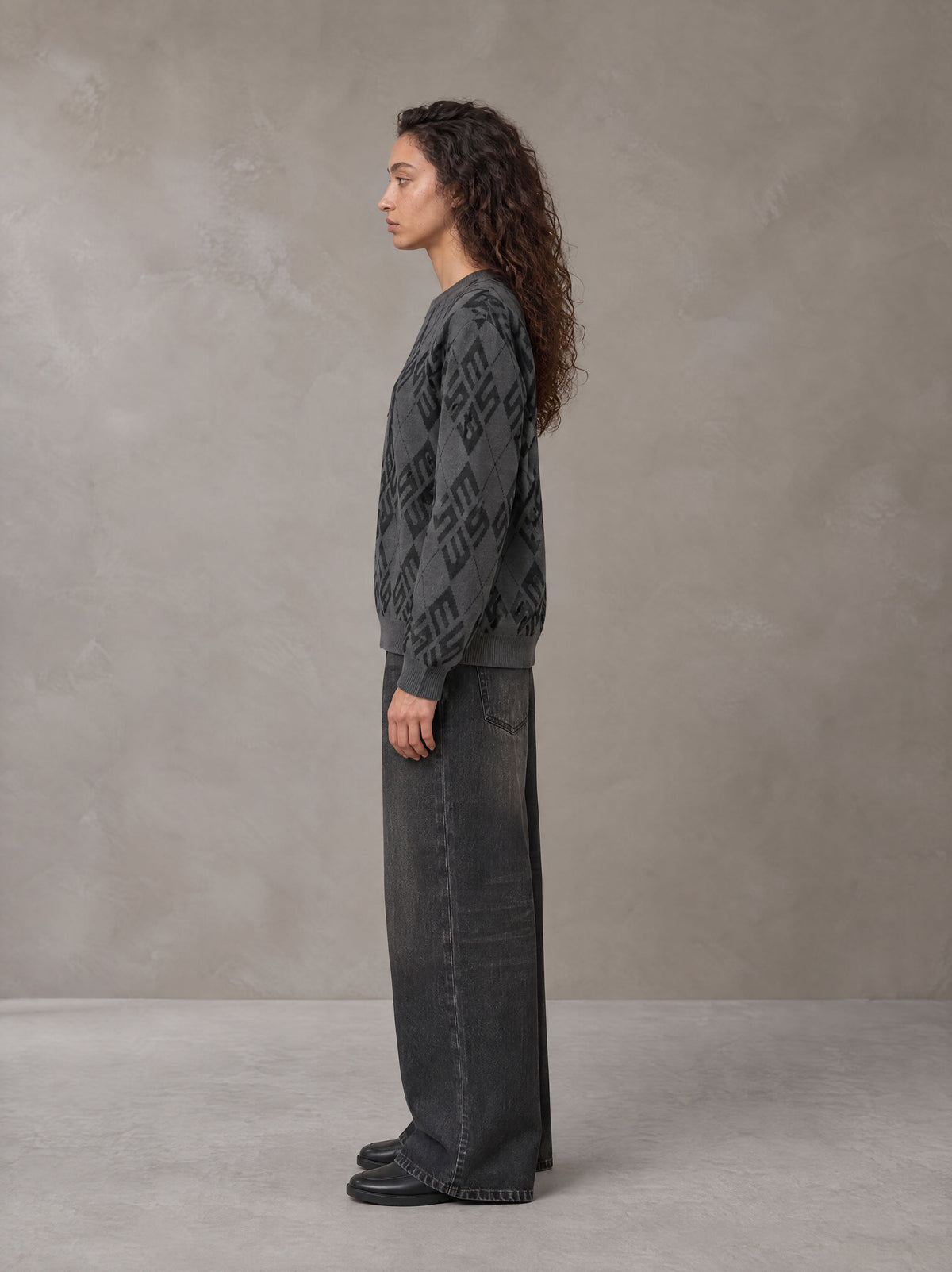 Model wearing the SM Argyle Jacquard Knitted Sweatshirt in Deep Charcoal, side profile.