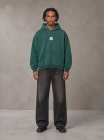 Model wearing the SM Monkey Wash Hoodie in Alpine Green, front view.