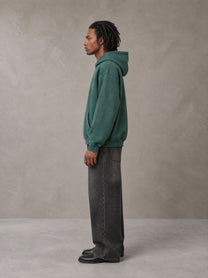 Model wearing the SM Monkey Wash Hoodie in Alpine Green, side profile.