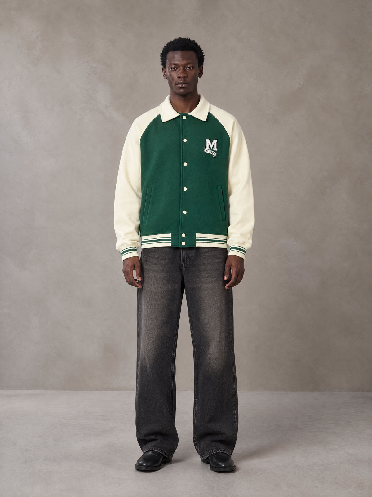 Model wearing the SM Varsity Baseball Jacket in Eden Green, front view.