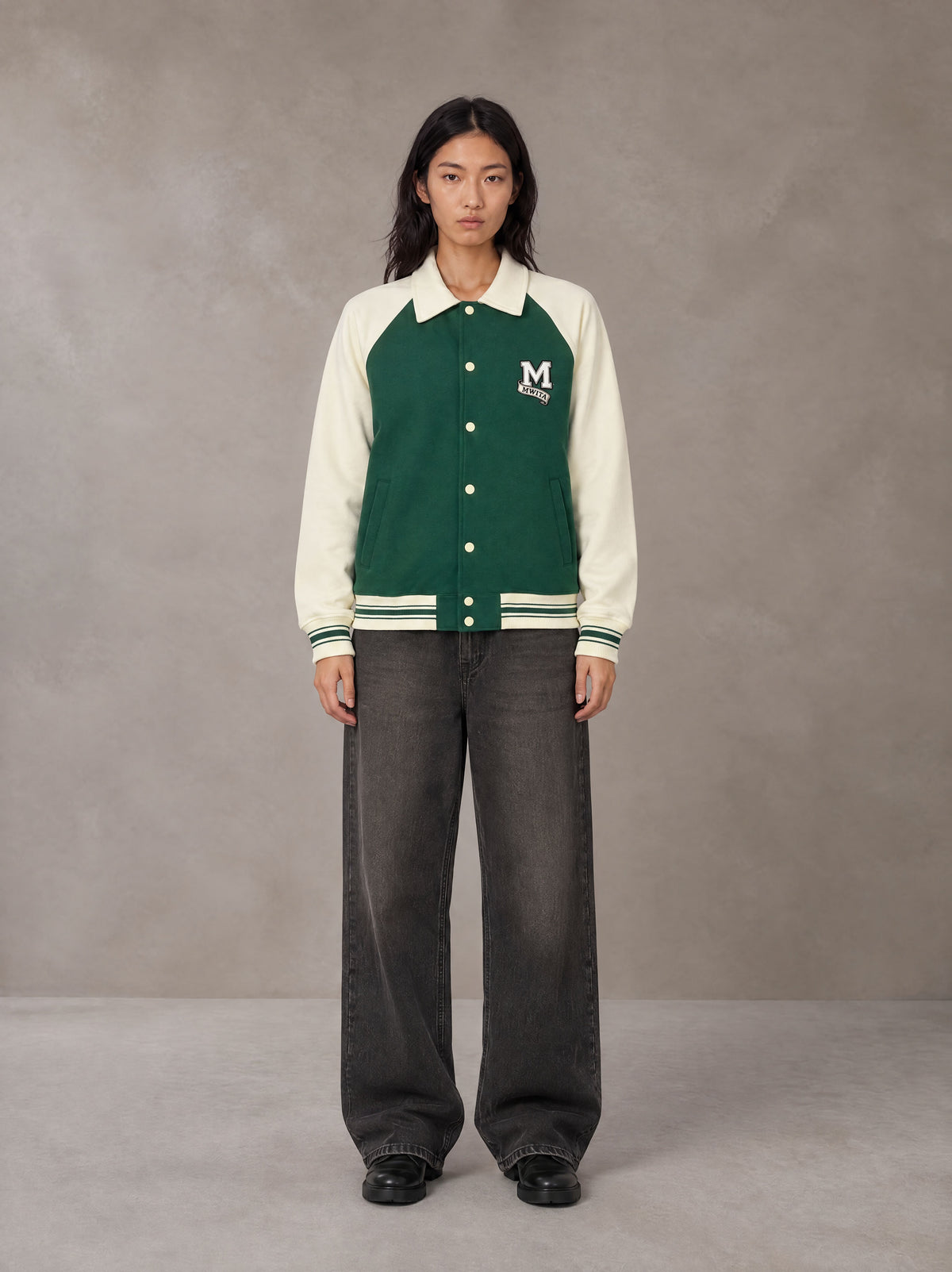 Model wearing the SM Varsity Baseball Jacket in Eden Green, front view.