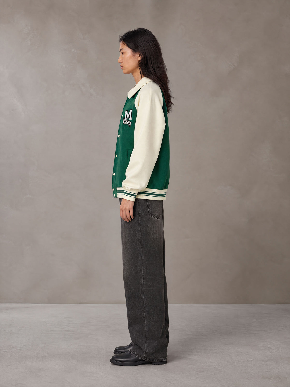 Model wearing the SM Varsity Baseball Jacket in Eden Green, side profile.