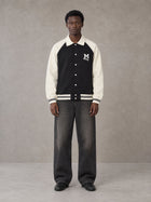 Model wearing the SM Varsity Baseball Jacket in Midnight Black, front view.