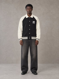 Model wearing the SM Varsity Baseball Jacket in Midnight Black, front view.