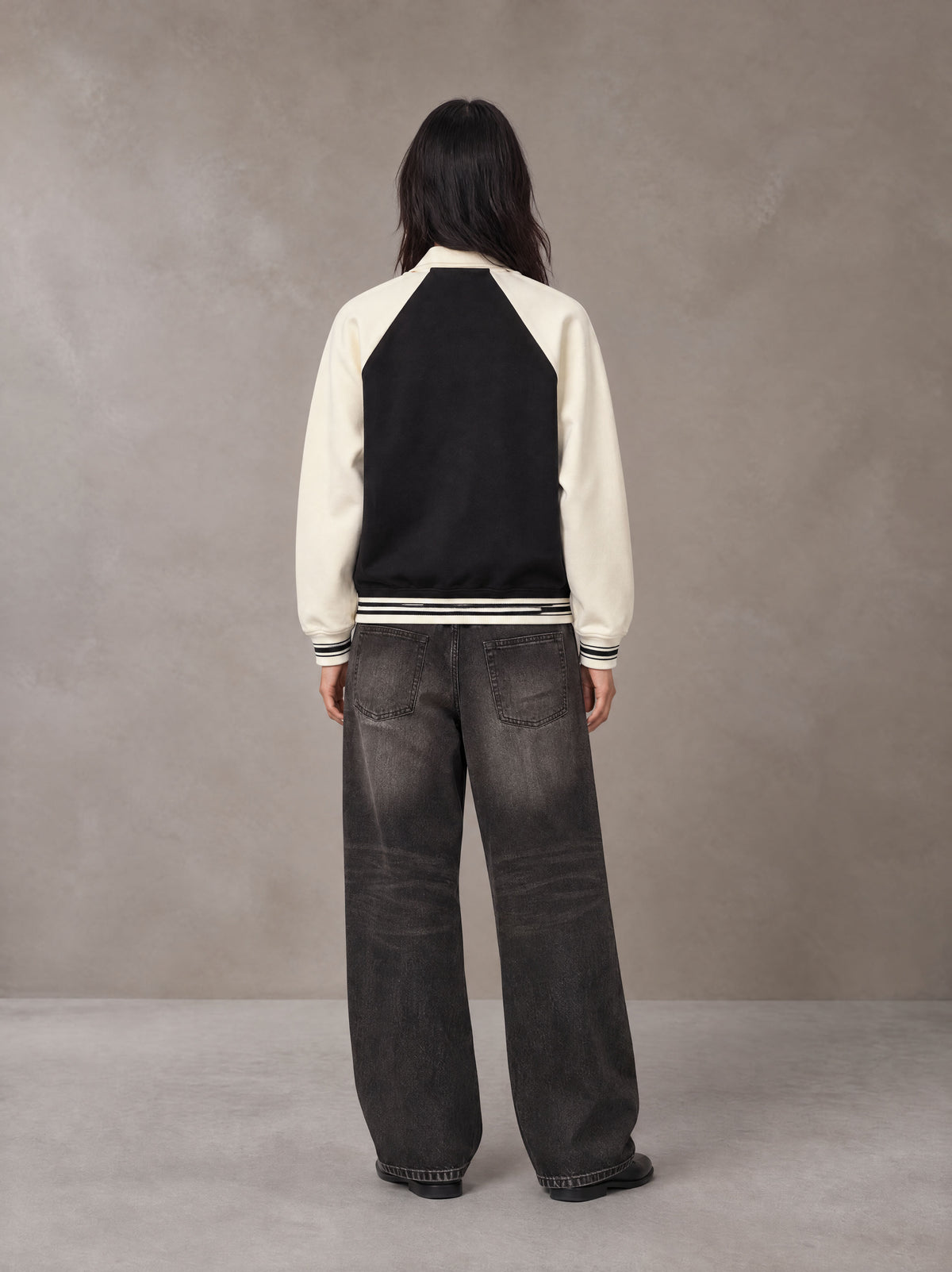 Model wearing the SM Varsity Baseball Jacket in Midnight Black, rear view.