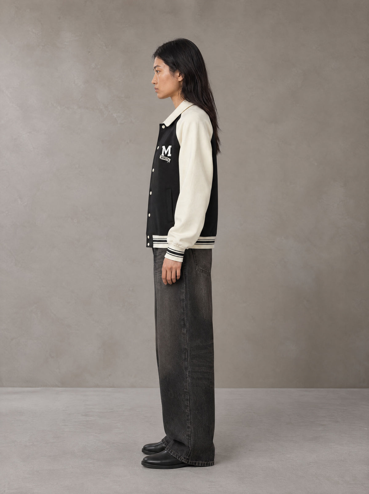 Model wearing the SM Varsity Baseball Jacket in Midnight Black, side profile.
