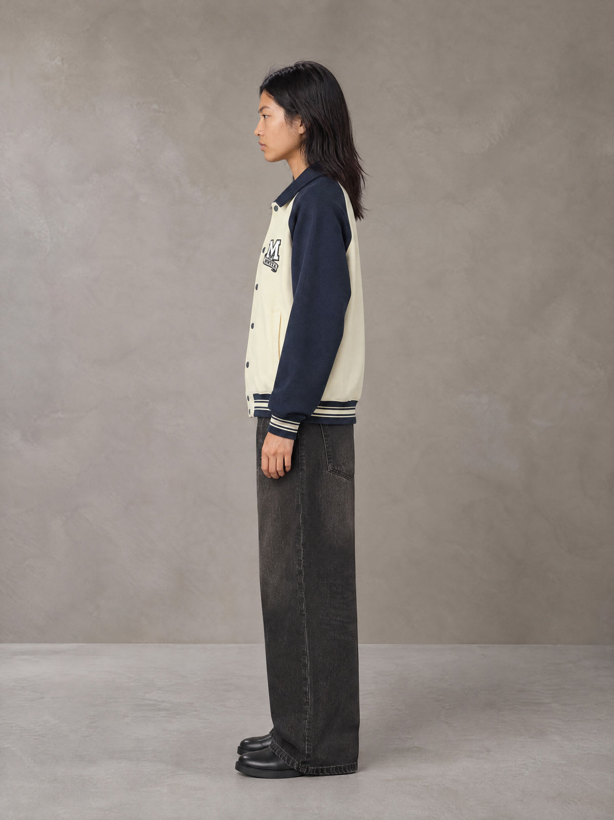 Model wearing the SM Varsity Baseball Jacket in Oxford Navy, side profile.