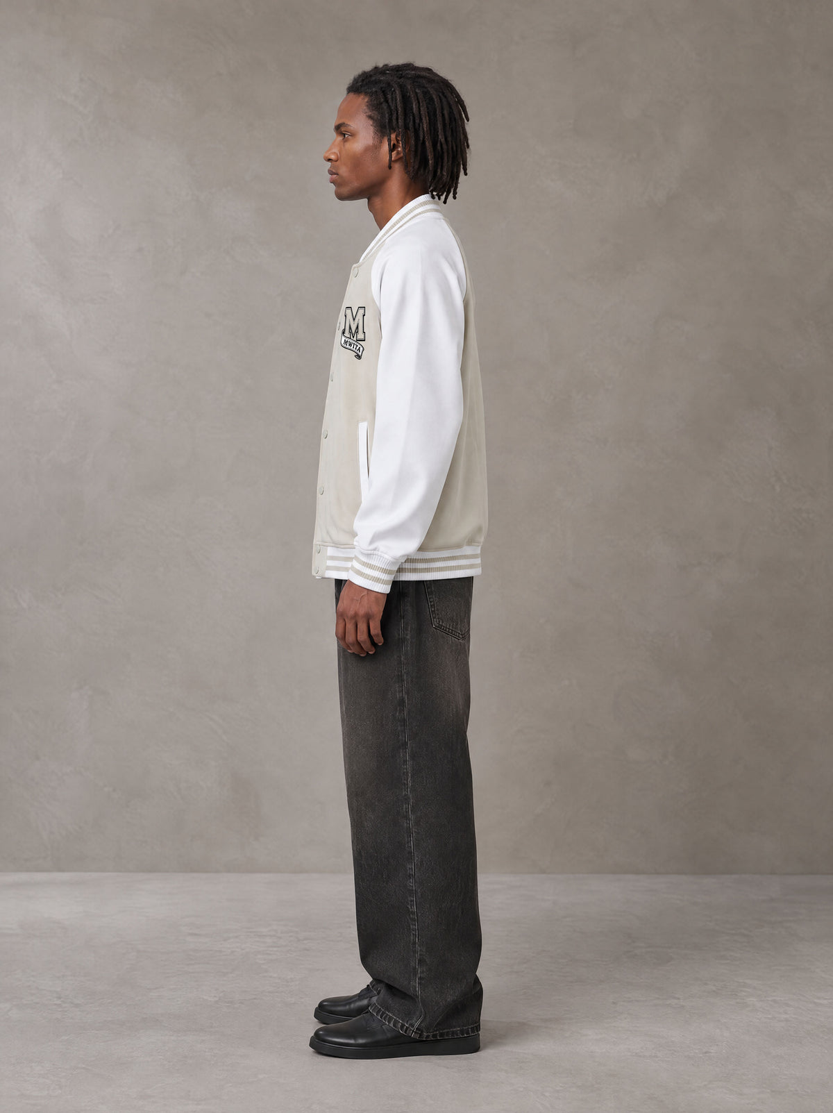 Model wearing the SM Varsity Jacket in Oatmeal Cookie, side profile.