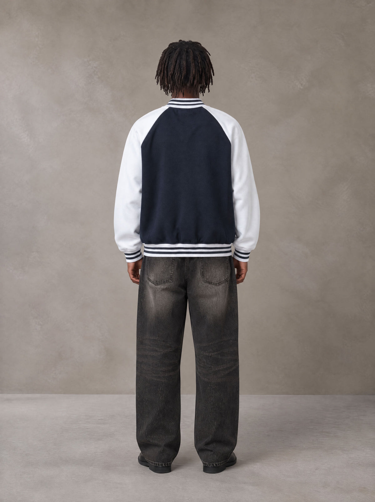 Model wearing the SM Varsity Jacket in Oxford Navy, rear view.